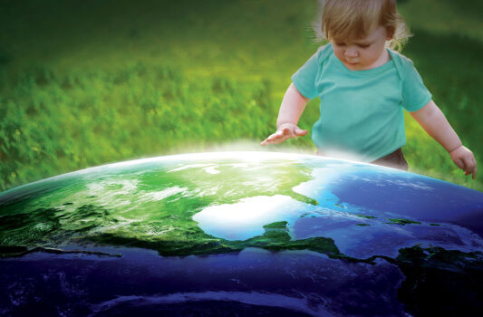 Kleinkind schaut hoffnungsvoll auf eine Weltkugel - im Hintergrund grüne Wiese